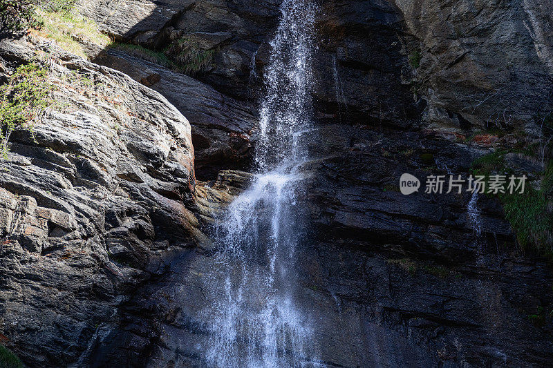 意大利奥斯塔山谷，Lillaz瀑布(Cascate di Lillaz)的瀑布飞溅在高山岩石的花岗岩壁架上，向阳一侧植被稀疏